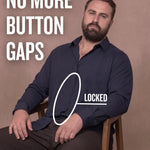 White man sitting on a chair wearing a navy long-sleeve dress shirt, pointing at the button placket to show no button gap, front view