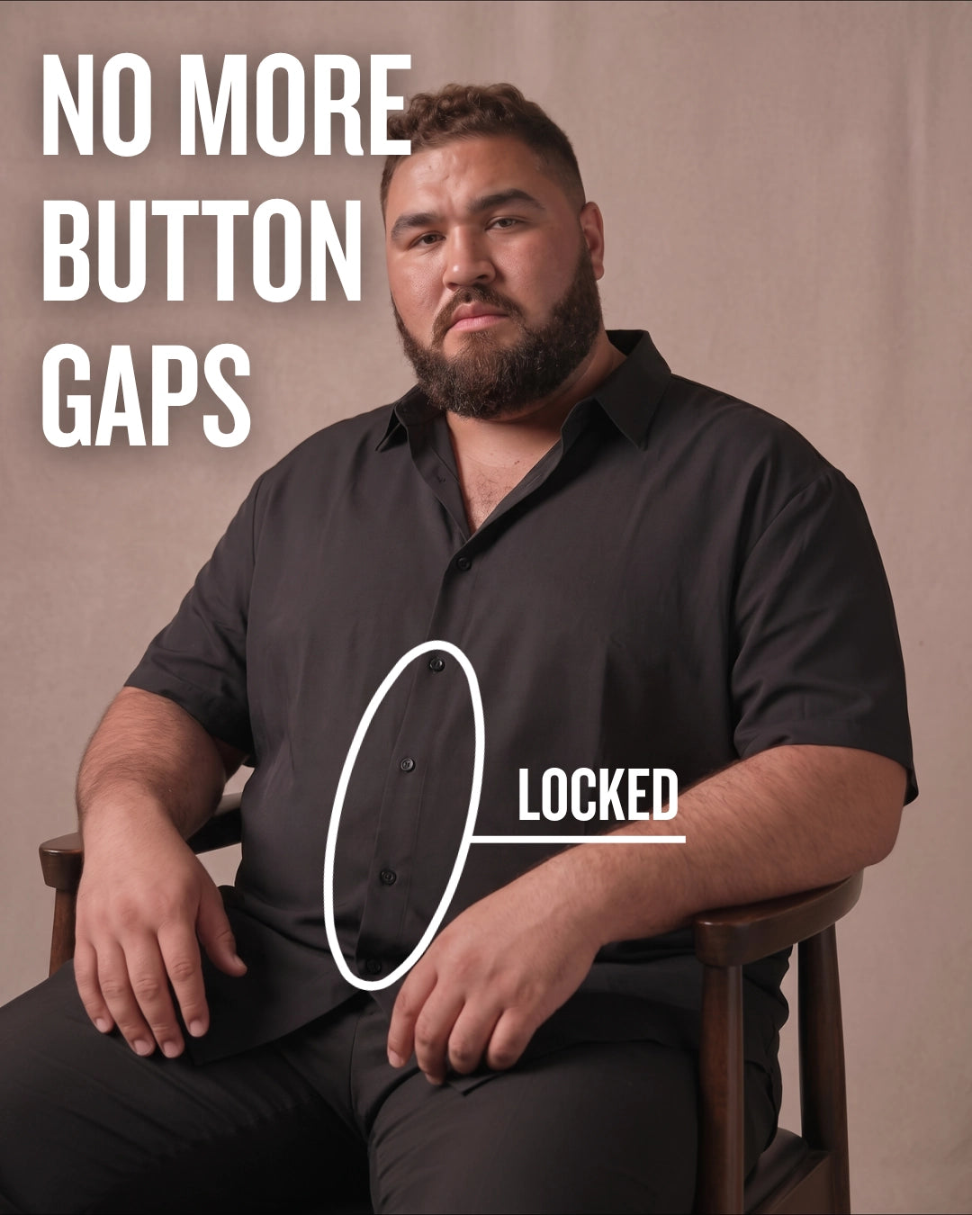 White man sitting on a chair wearing a black short-sleeve dress shirt, pointing at the button placket to show no button gap, front view