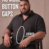 White man sitting on a chair wearing a black short-sleeve dress shirt, pointing at the button placket to show no button gap, front view