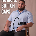 White man sitting on a chair wearing a light blue short-sleeve dress shirt, pointing at the button placket to show no button gap, front view