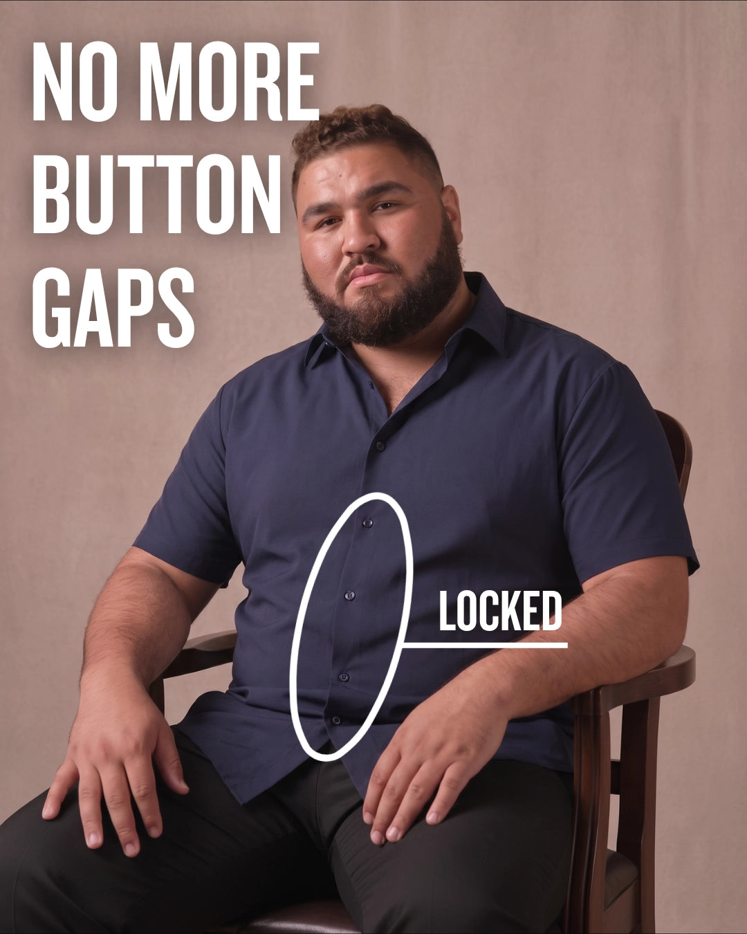 White man sitting on a chair wearing a navy short-sleeve dress shirt, pointing at the button placket to show no button gap, front view