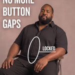 Black man sitting on a chair wearing a black short-sleeve dress shirt, pointing at the button placket to show no button gap, front view