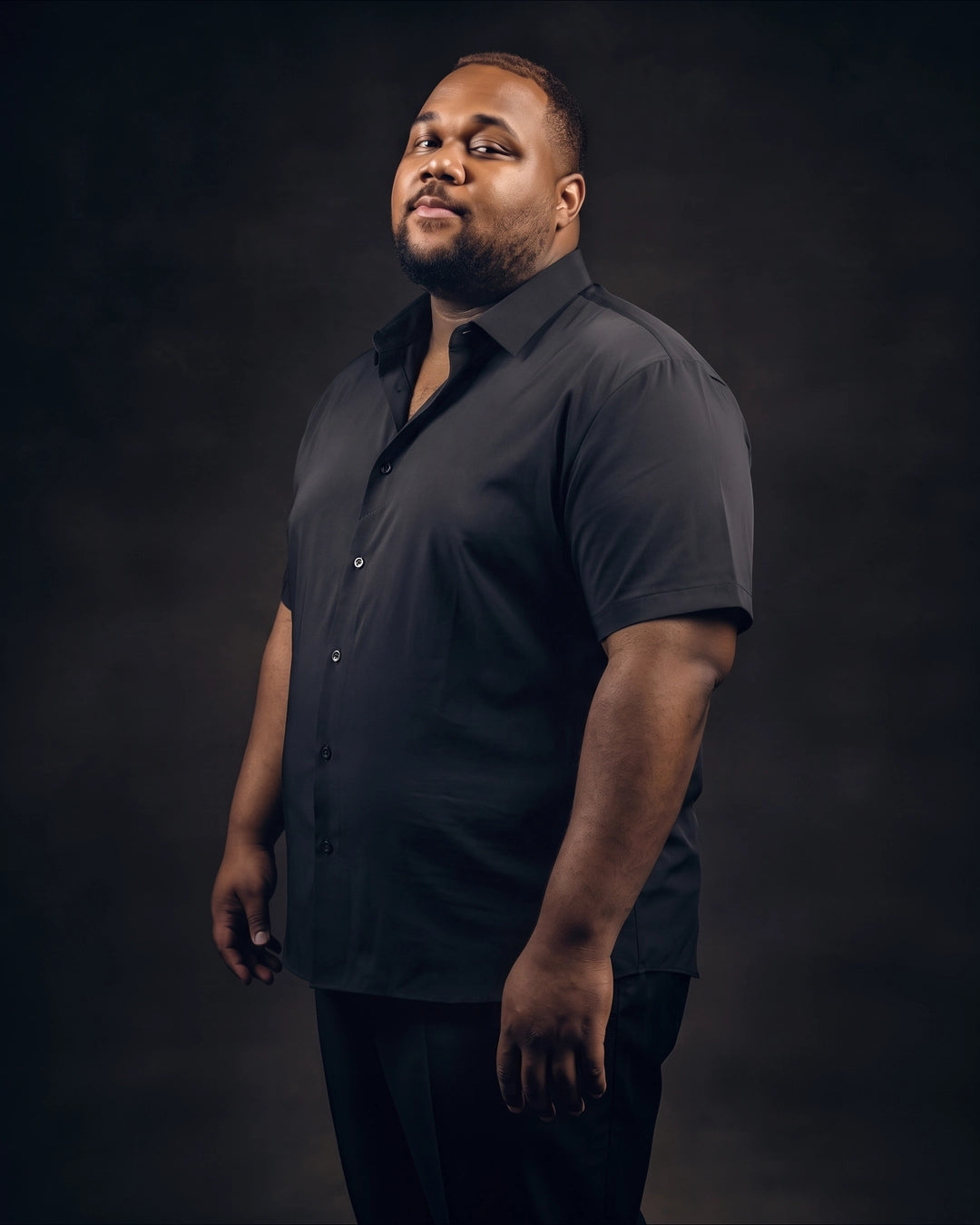 Plus-size Black man trying on NEVER GAPE No-Gap Stretch Dress Shirt in Black, Short Sleeve, side view