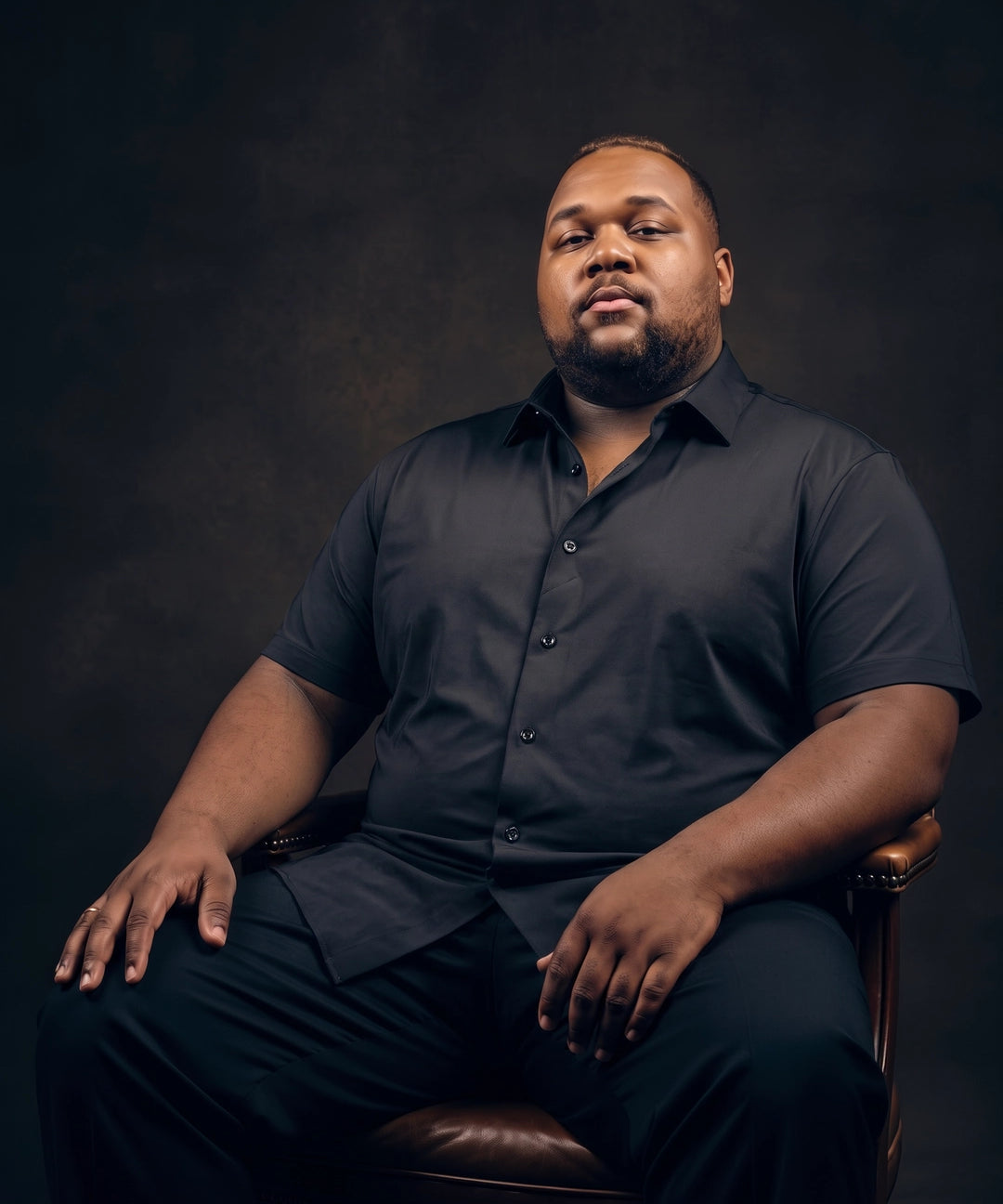 Plus-size Black man sitting in a chair wearing NEVER GAPE No-Gap Stretch Dress Shirt in Black, Short Sleeve
