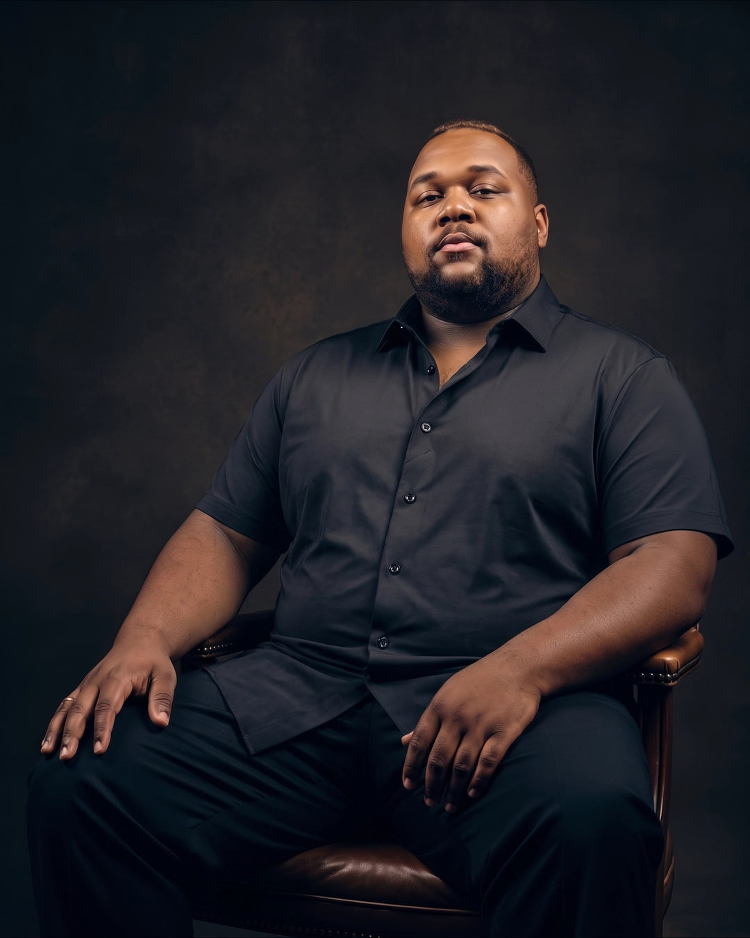 Plus-size Black man sitting in a chair wearing NEVER GAPE No-Gap Stretch Dress Shirt in Black, Short Sleeve