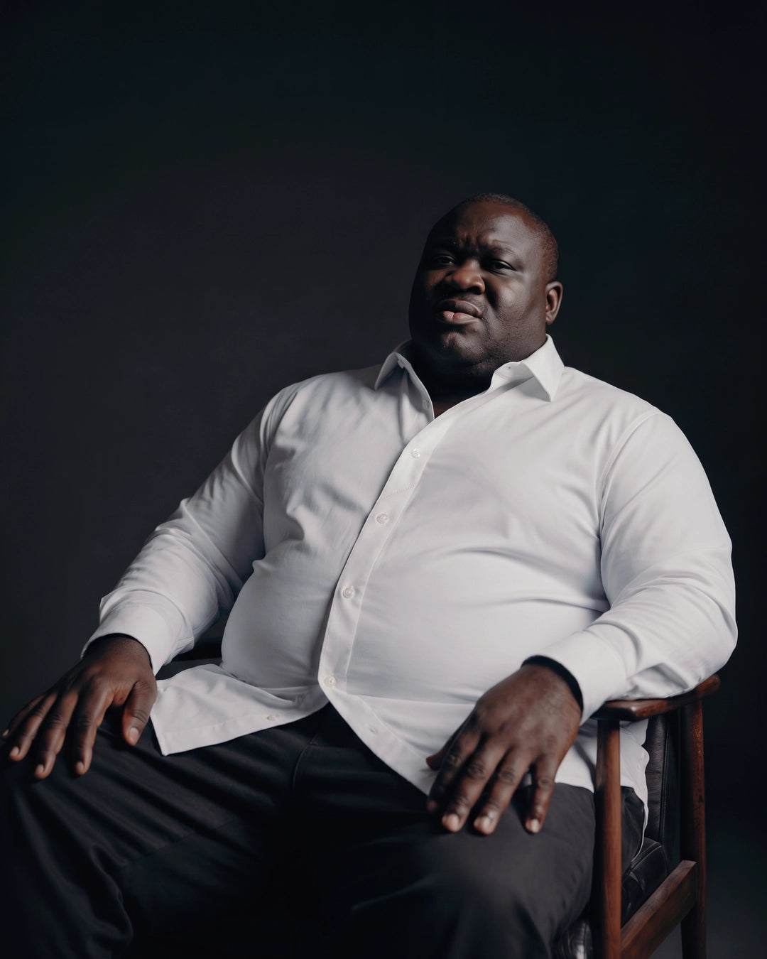 Plus-size Black man sitting in a chair wearing NEVER GAPE No-Gap Stretch Dress Shirt in White, Long Sleeve