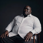 Plus-size Black man sitting in a chair wearing NEVER GAPE No-Gap Stretch Dress Shirt in White, Long Sleeve