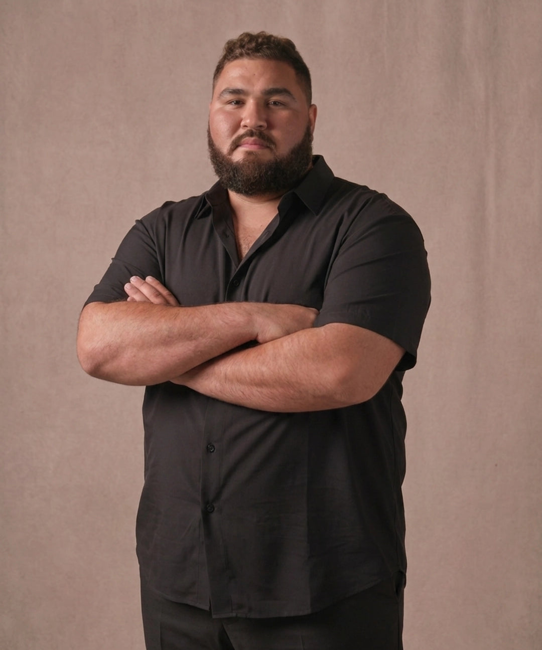 White man wearing a black short-sleeve dress shirt with arm clossed, front view